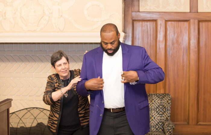 A man in a purple jacket is helping a woman put on a purple jacket.